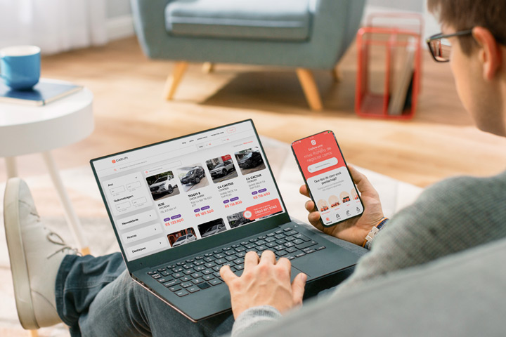 Rapaz sentado em sofá de sua casa acessando plataforma da Carupi em seu notebook e em celular