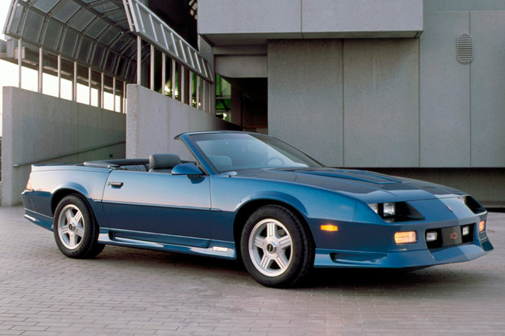 Chevrolet Camaro azul conversível ano 1992 estacionado em frente a prédio de concreto