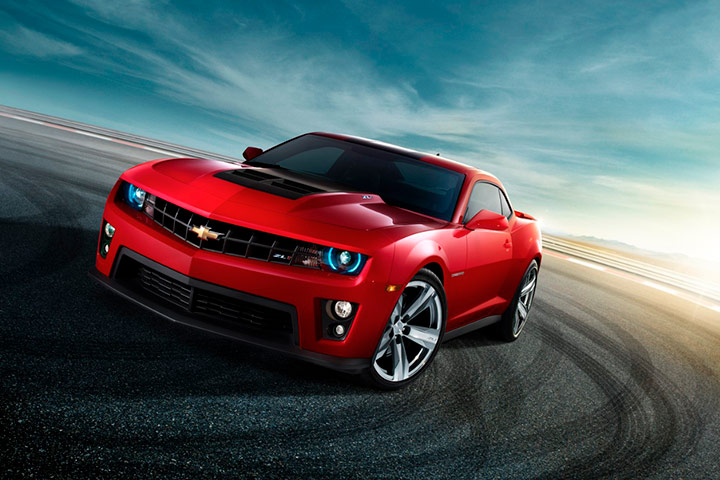 Chevrolet Camaro 2012 vermelho em piso de asfalto com marcas de derrapagem e céu de entardecer ao fundo