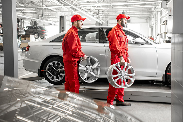 Dois mecânicos uniformizados em grande oficina mecânica de concessionária segurando rodas de carros
