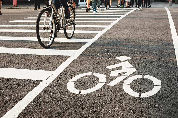 Faixa de pedestres e símbolo de ciclovia pintados em rua com pessoas atravessando