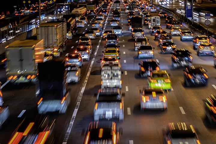 Visão aérea de grande avenida em metrópole com carros passando e deixando rastros de luz de seus faróis