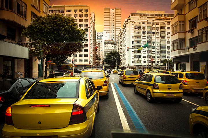Rua movimentada do Rio de Janeiro com diversos táxis amarelos parados um ao lado do outro no sinal vermelho