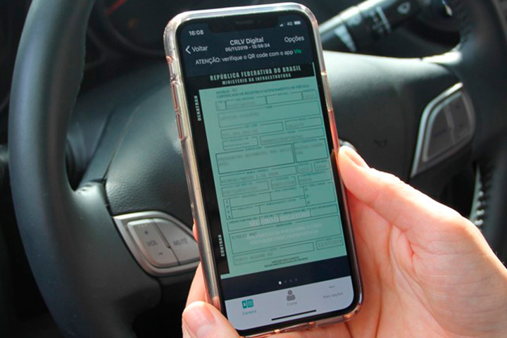 Mão segurando celular com documento digital do carro aberto e volante do veículo ao fundo