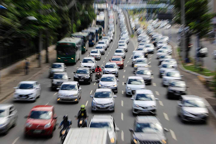 Grande avenida de cidade com diversas faixas de trânsito repleta de carros em fila congestionados