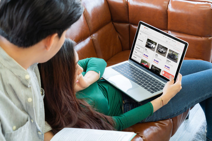 Jovem casal relaxando em sofá de casa com computador aberto acessando website da Carupi
