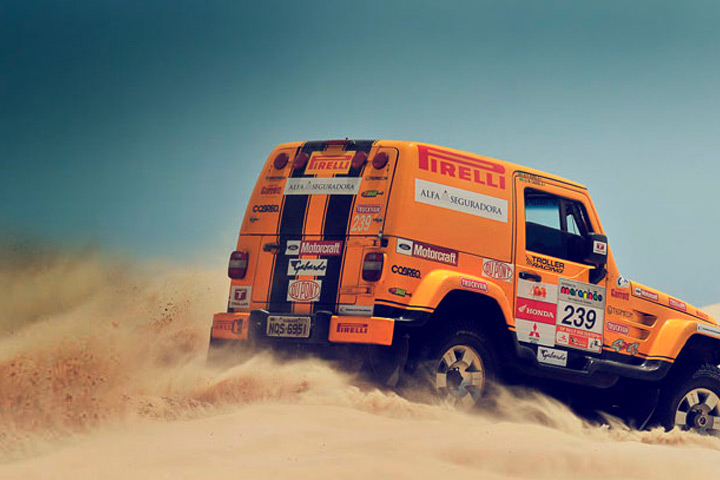 Jipe Troller T4 amarelo coberto de adesivos de patrocinadores atravessando duna de deserto em rally