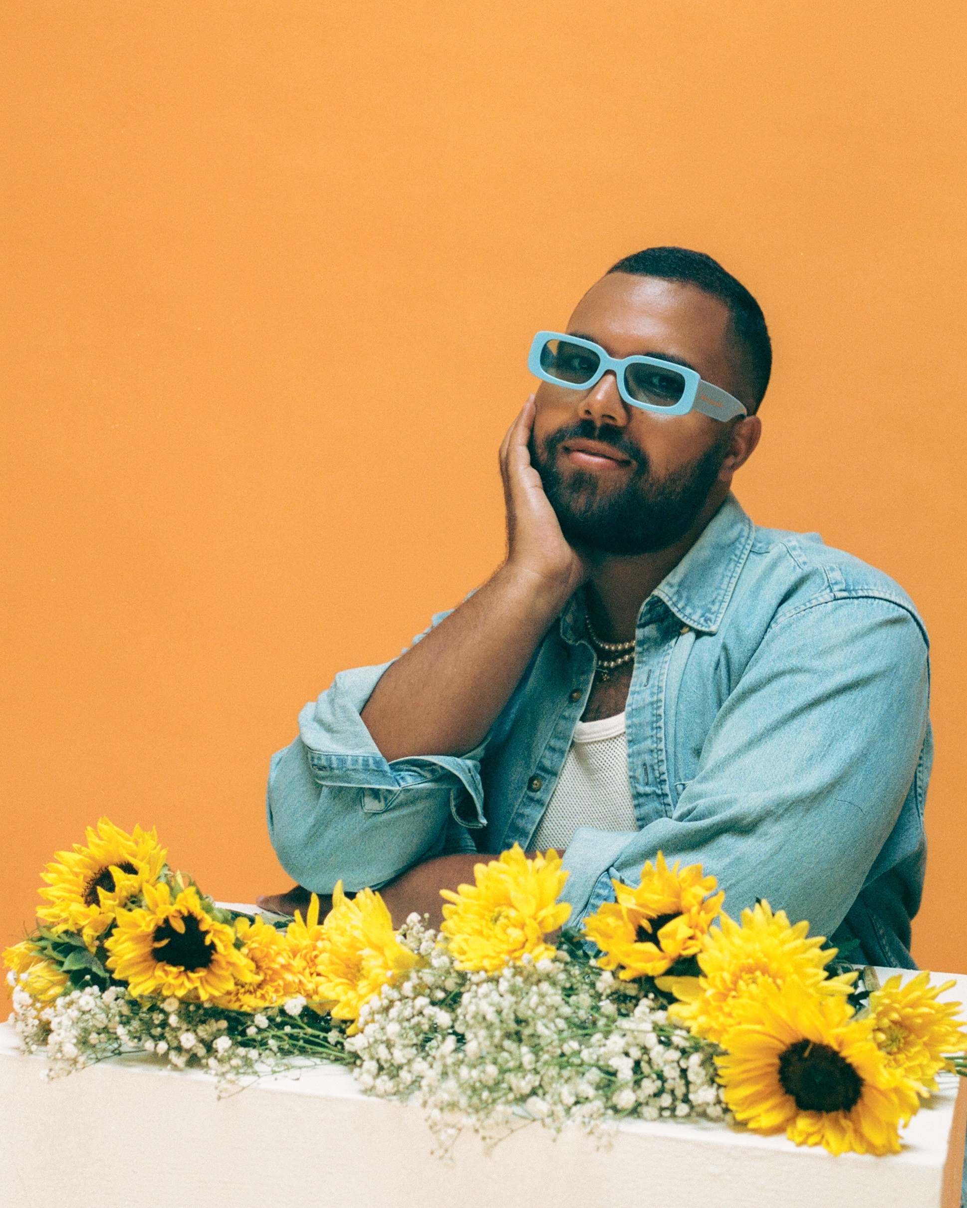 A portrait of Micah wearing sunglasses and holding sunflowers