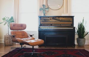 Piano in a living room behind a tan chair. Among the things to consider before moving your piano is if your new place has enough room for it.