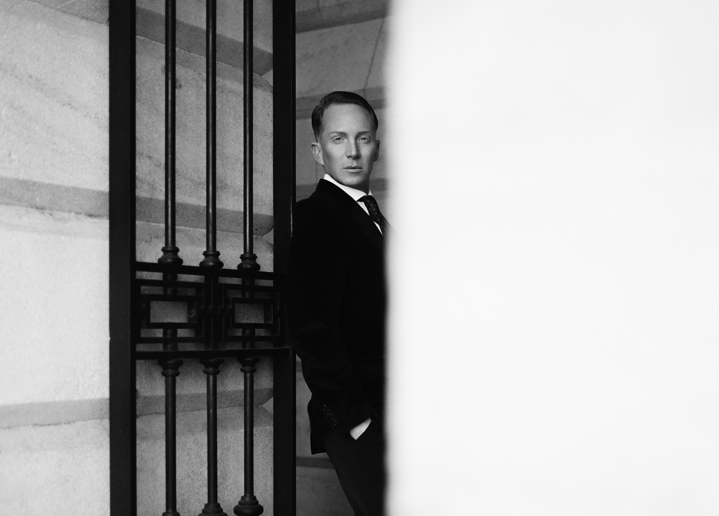 Partially obscured black and white portrait of Paul Corrie leaning on an iron gate.
