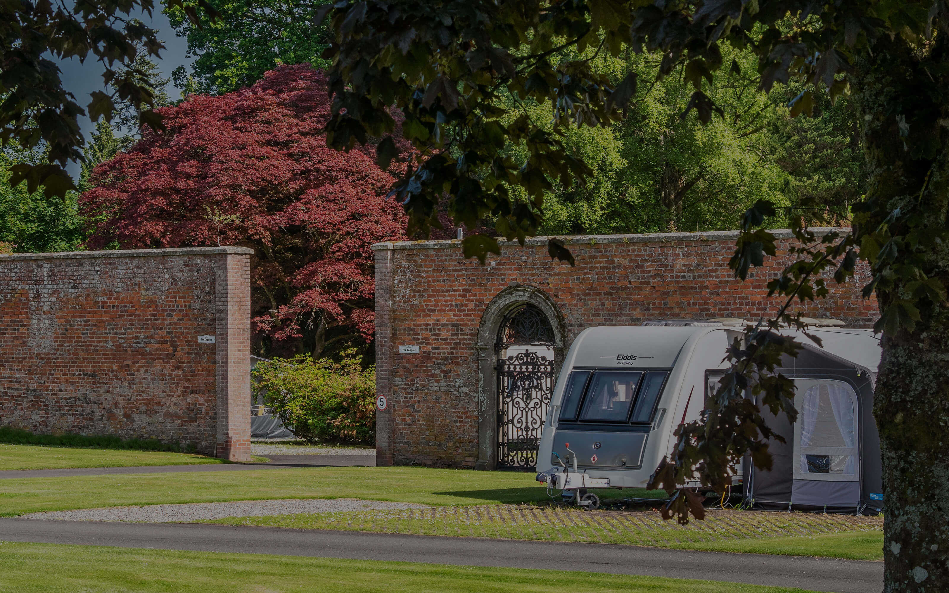 A caravan to the right of the walled garden entrance.