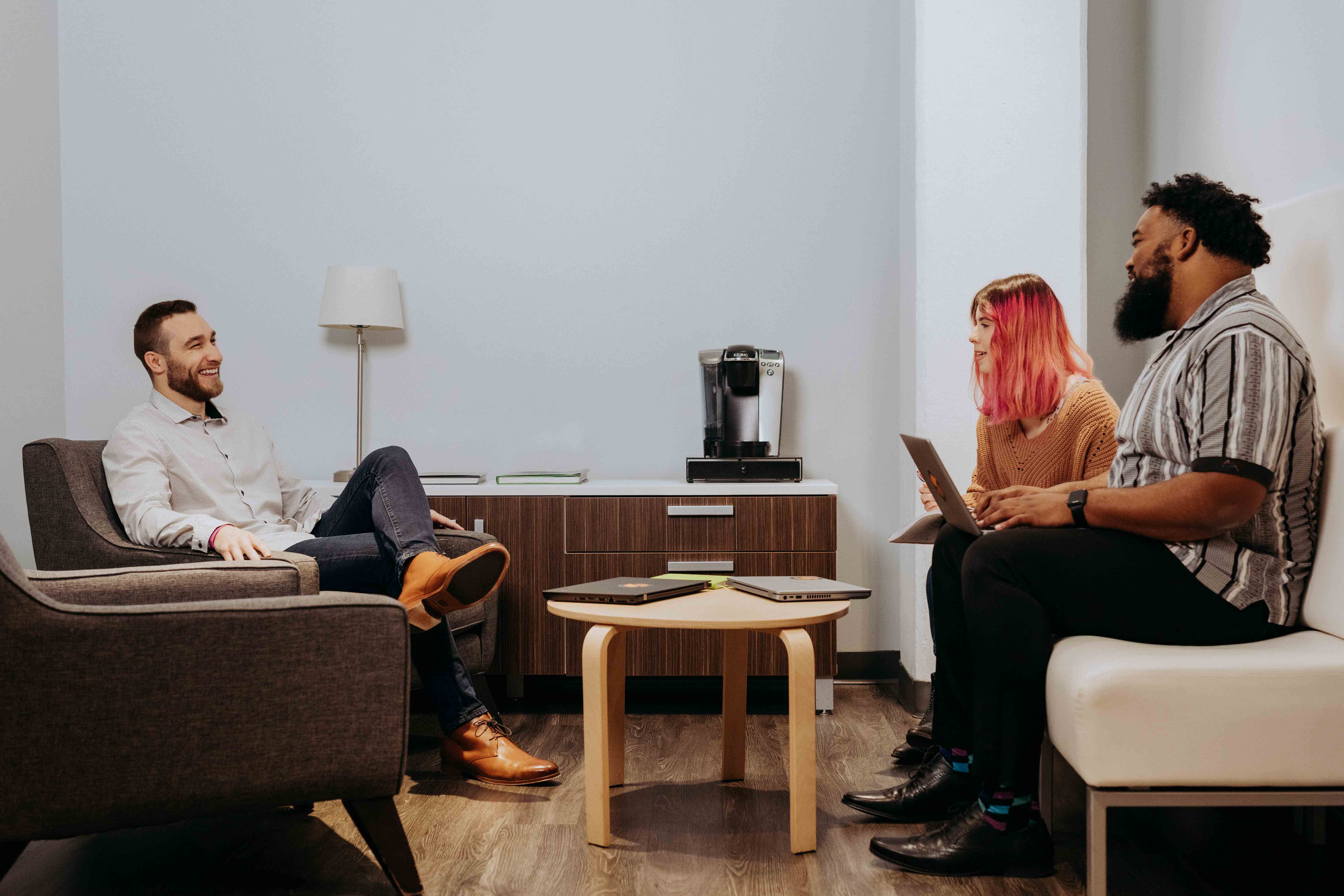 Three Steam Logistics employees meet in the break room while one takes notes on his laptop.