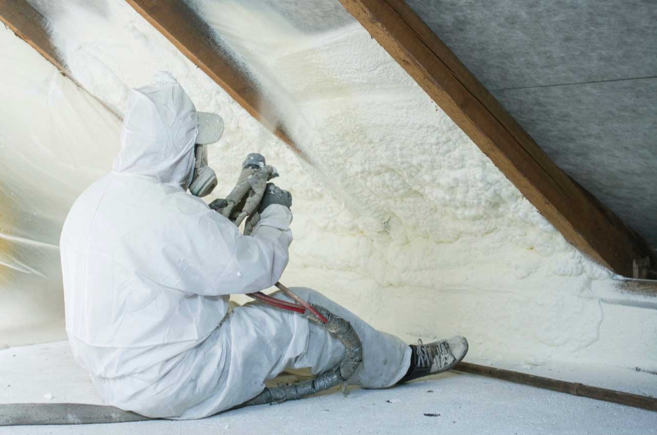 person in full protective clothing and mask spraying foam to insulate a loft