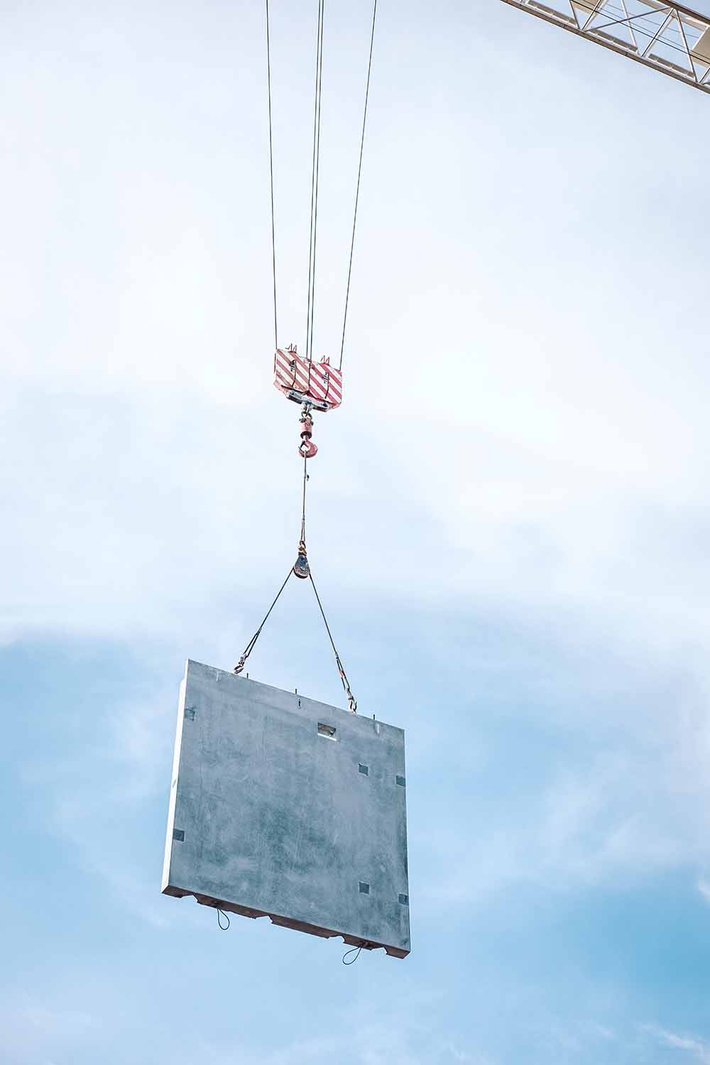 A precast concrete wall is hoisted up into the air by a crane.