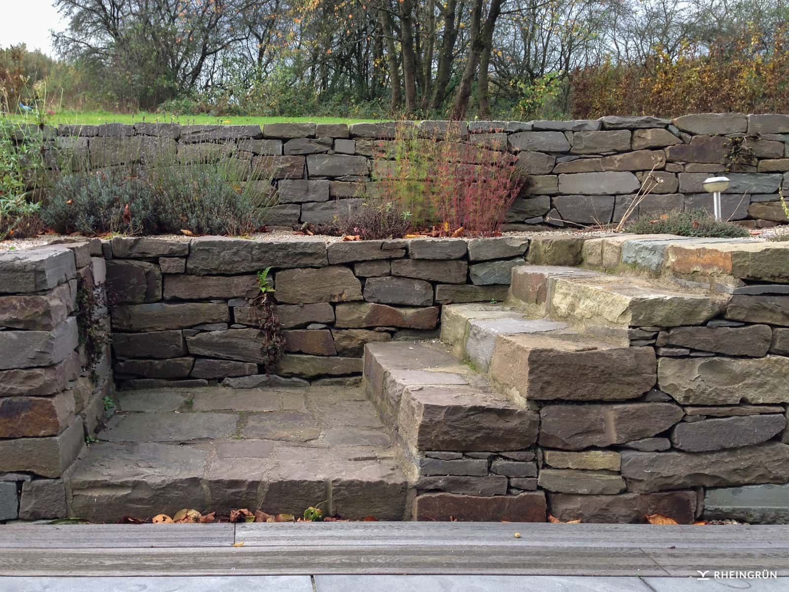 Rustikaler Privatgarten mit Terrasse und Mauer aus Grauwacke Rheingrün