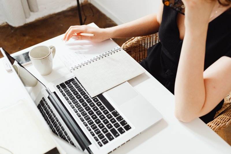 Person sitting at the desk, browsing on a laptop and taking notes on a notebook