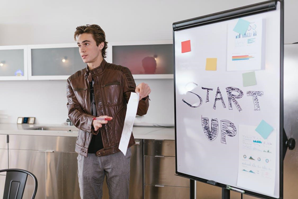 Man standing in front of white board presenting information about startup companies.