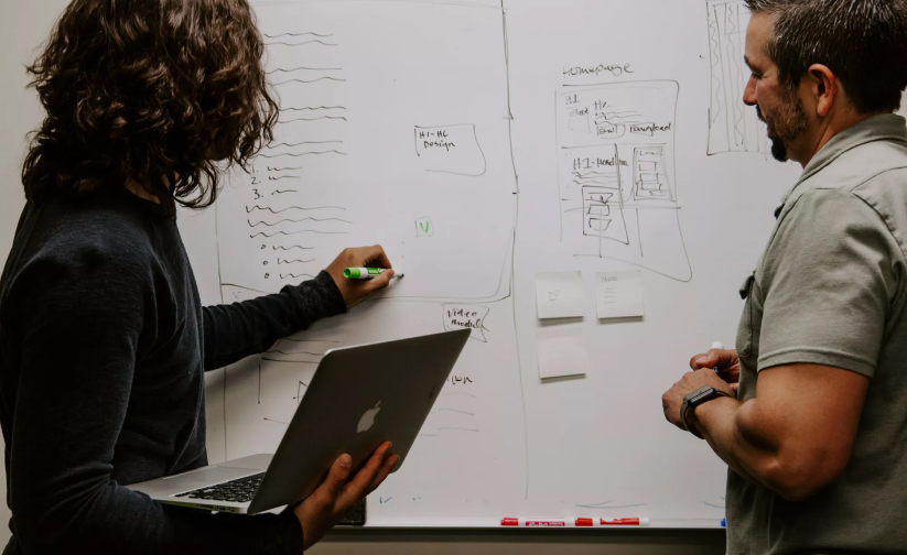 Two business growth program consultants whiteboard a client problem