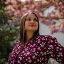 Ruchika stands in a garden with a blossoming tree behind her.