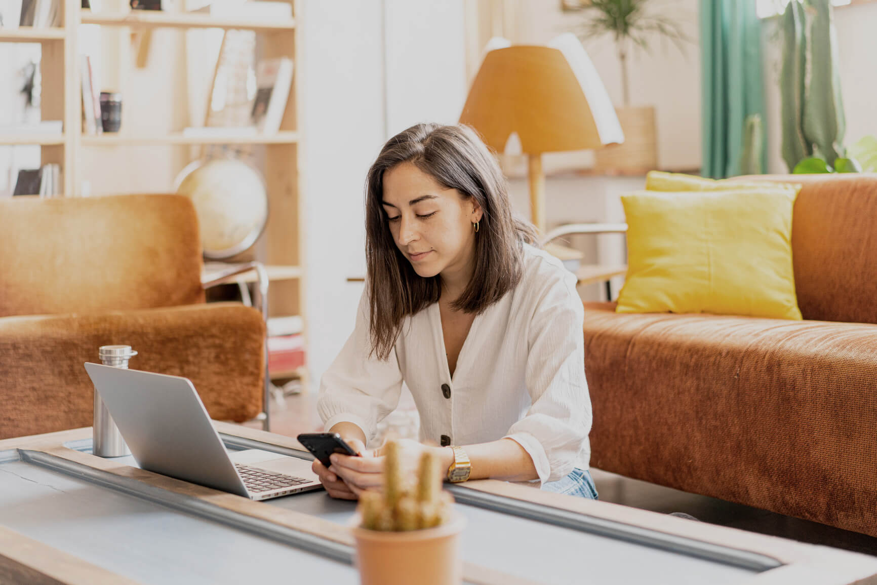 Middle age woman sitting on floor in front of laptop, while looking calmly at phone