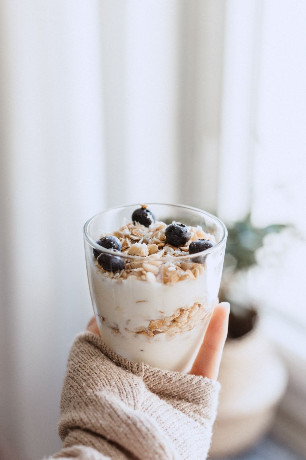 Mão segura copo cheio com iogurte, grãos e frutas