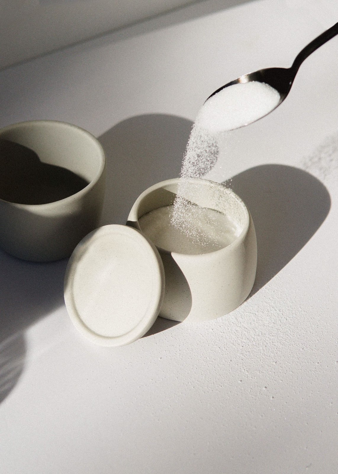 Colher retira açúcar de pote cor creme. Ao lado, há um pote vazio