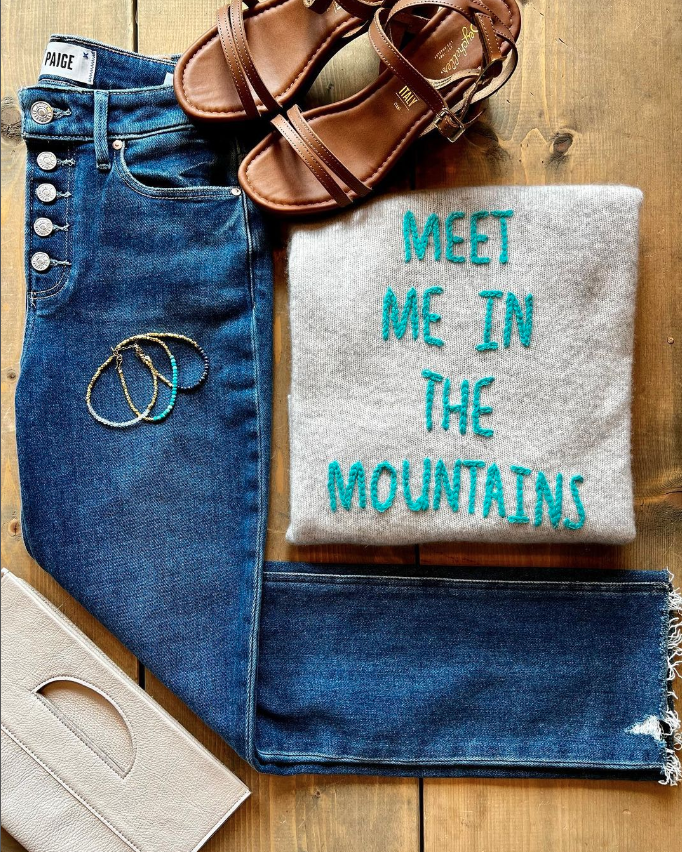 An outfit from Juniper Boutique next to a sweater that says "meet me in the mountains".