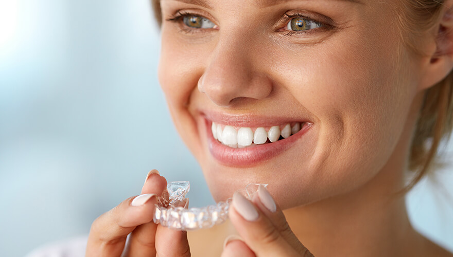 Woman smiling and holding a set of invisible braces in front of her mouth