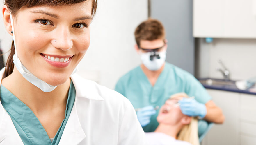 Closeup of a female dentist smiling while a male dentist is performing a dental filling on a patient