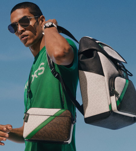 man in a green shirt wearing sunglasses with a side bag and michael kors backpack held over his shoulder.