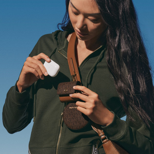 Young woman placing air pod case in a Michael Kors carrying pouch