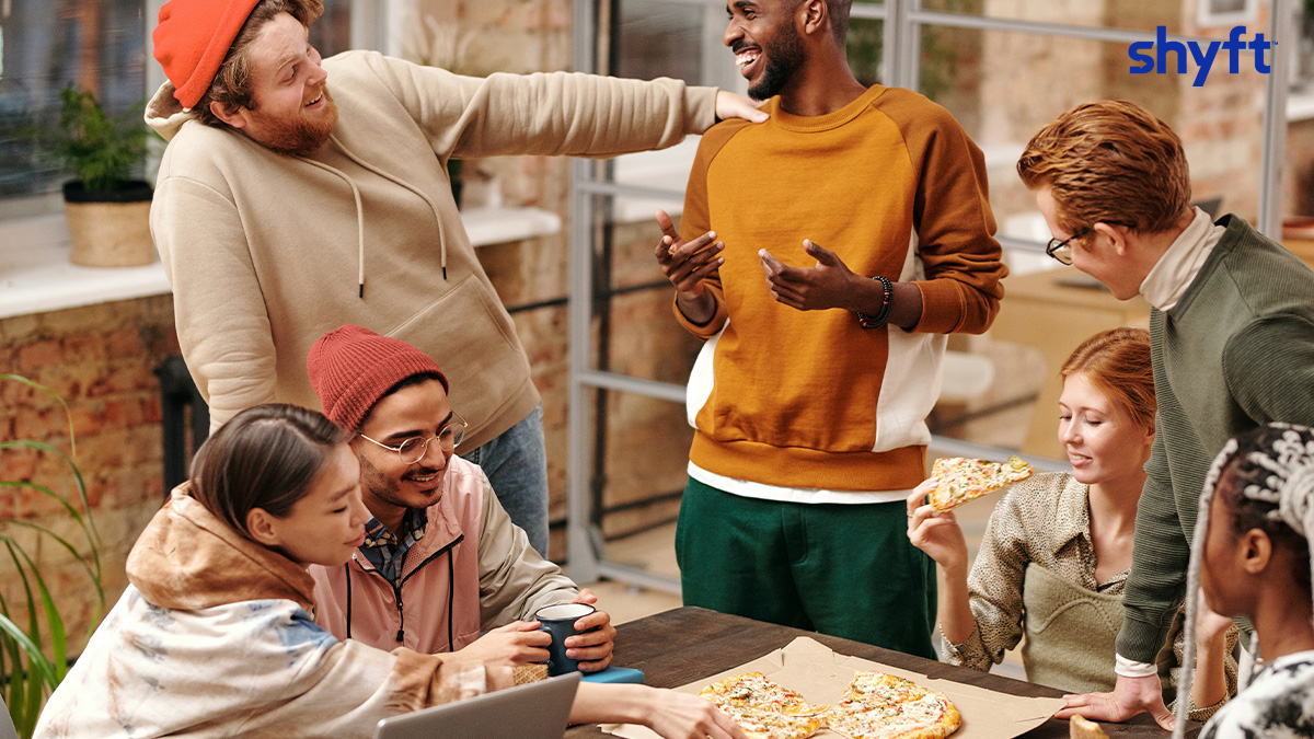 A group of people hanging out in the office drinking coffee and sharing a pizza 