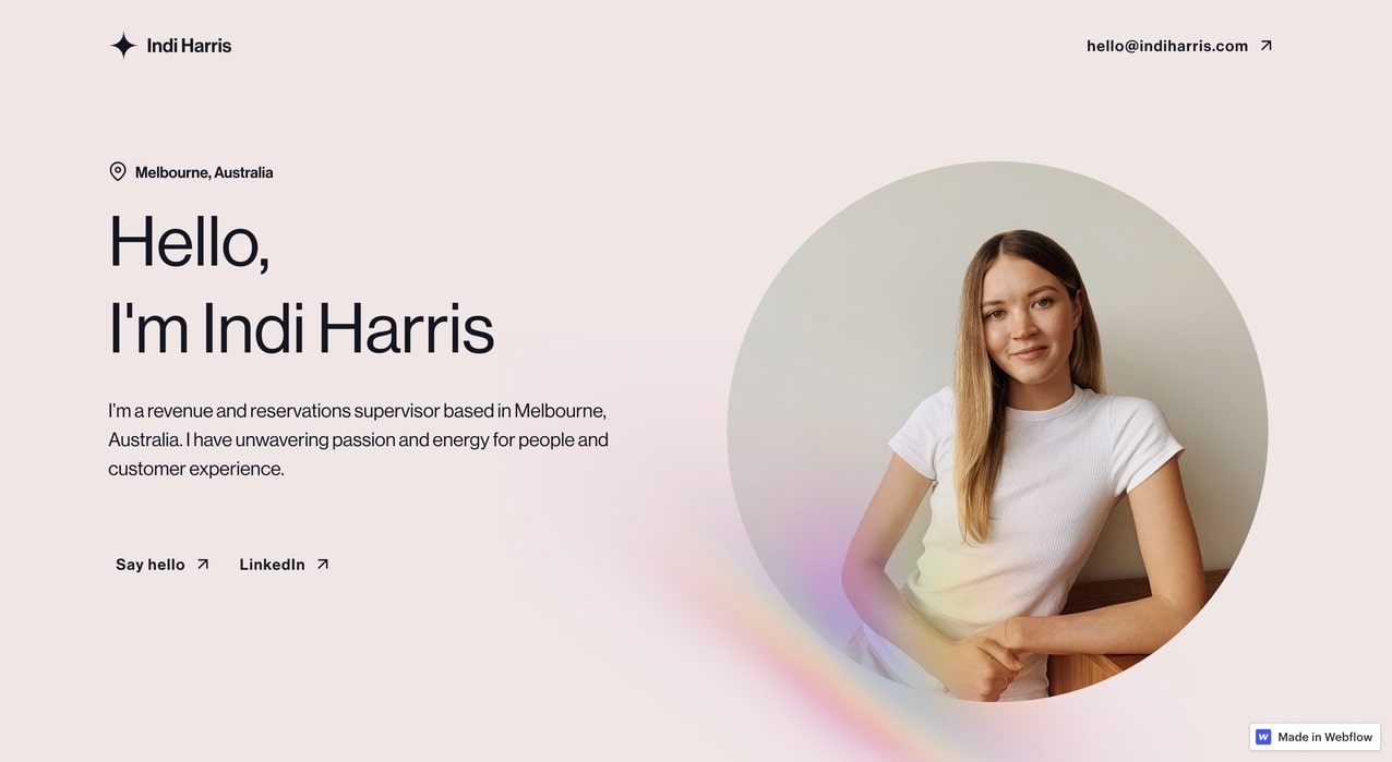 Indi Harris website. Blush background. Right side features a large beige circle with a photo of Indi inside. Subtle rainbow light on the bottom outer edge of the circle. Left side has text "Hello, I'm Indi Harris."