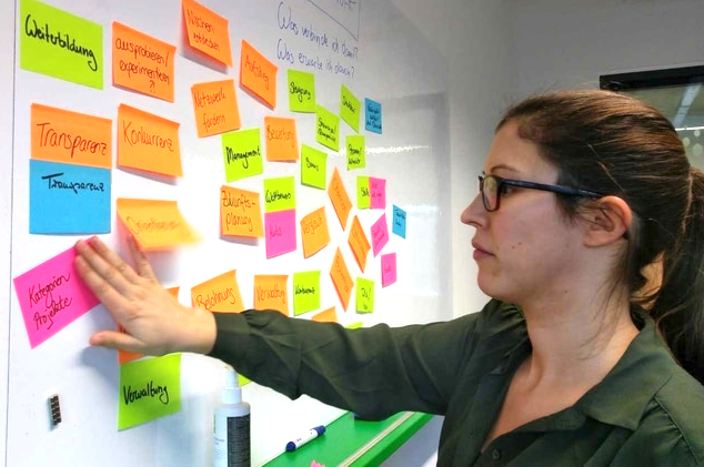 Frau steht am Whiteboard und betrachtet bunte Postits