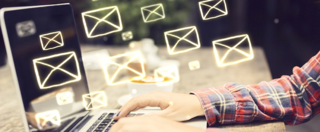 Man typing on a laptop with email symbols surround the keyboard to show he's sending emails