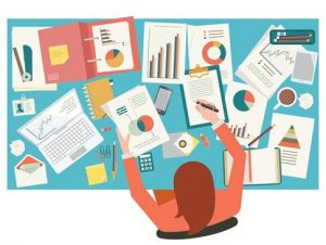 Busy workplace desk with stats, graphs, and papers scattered around the surface