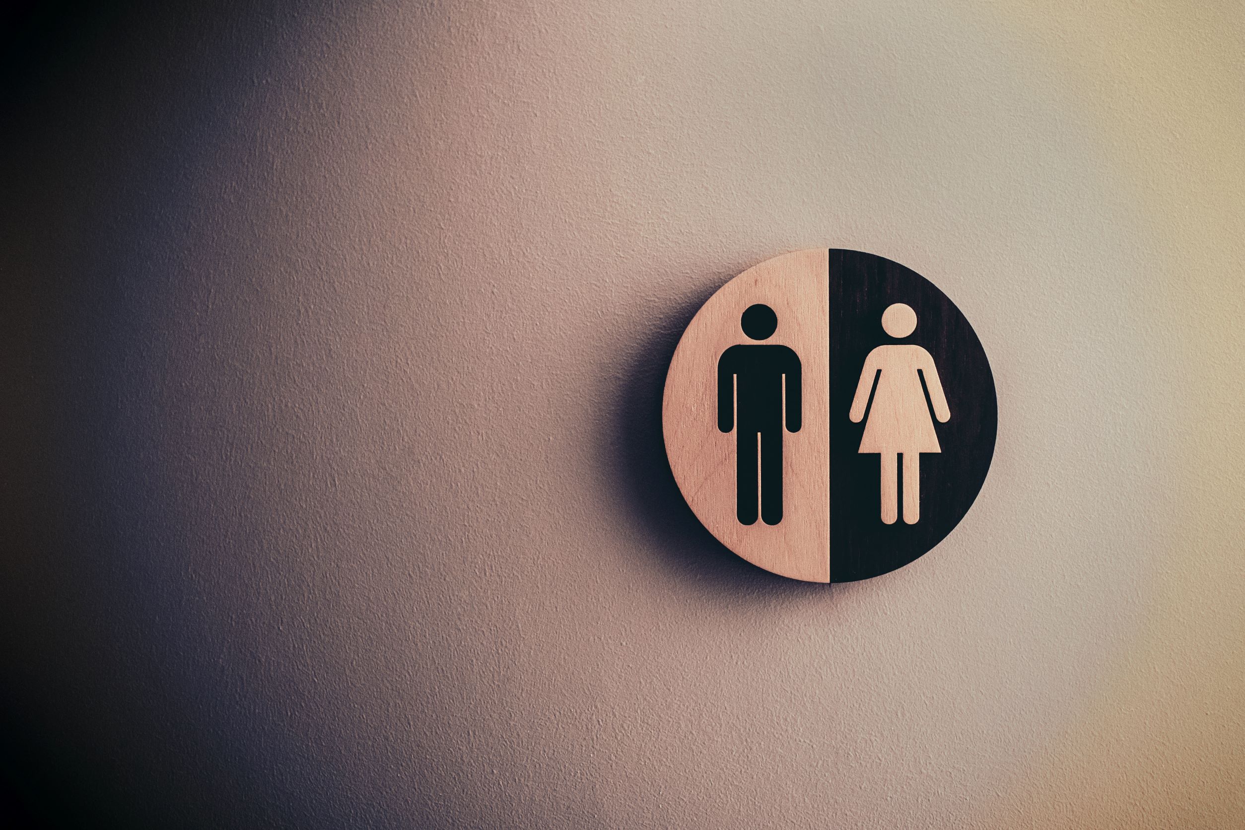 Round sign with an outline of a woman in white on a black background and an outline of a man in black on a white background