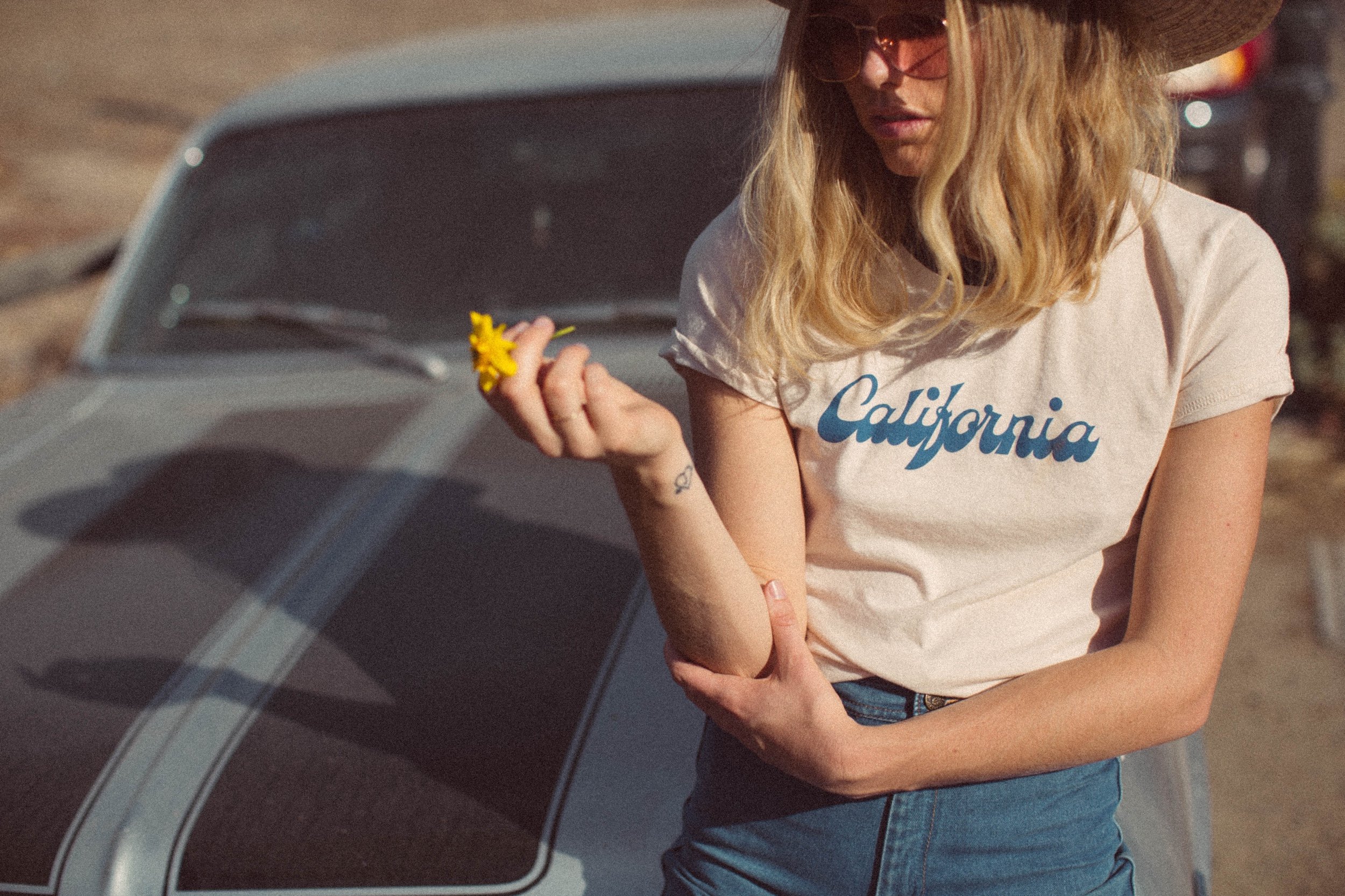 Image of a model sitting on a car wearing a t-shirt that reads "California"