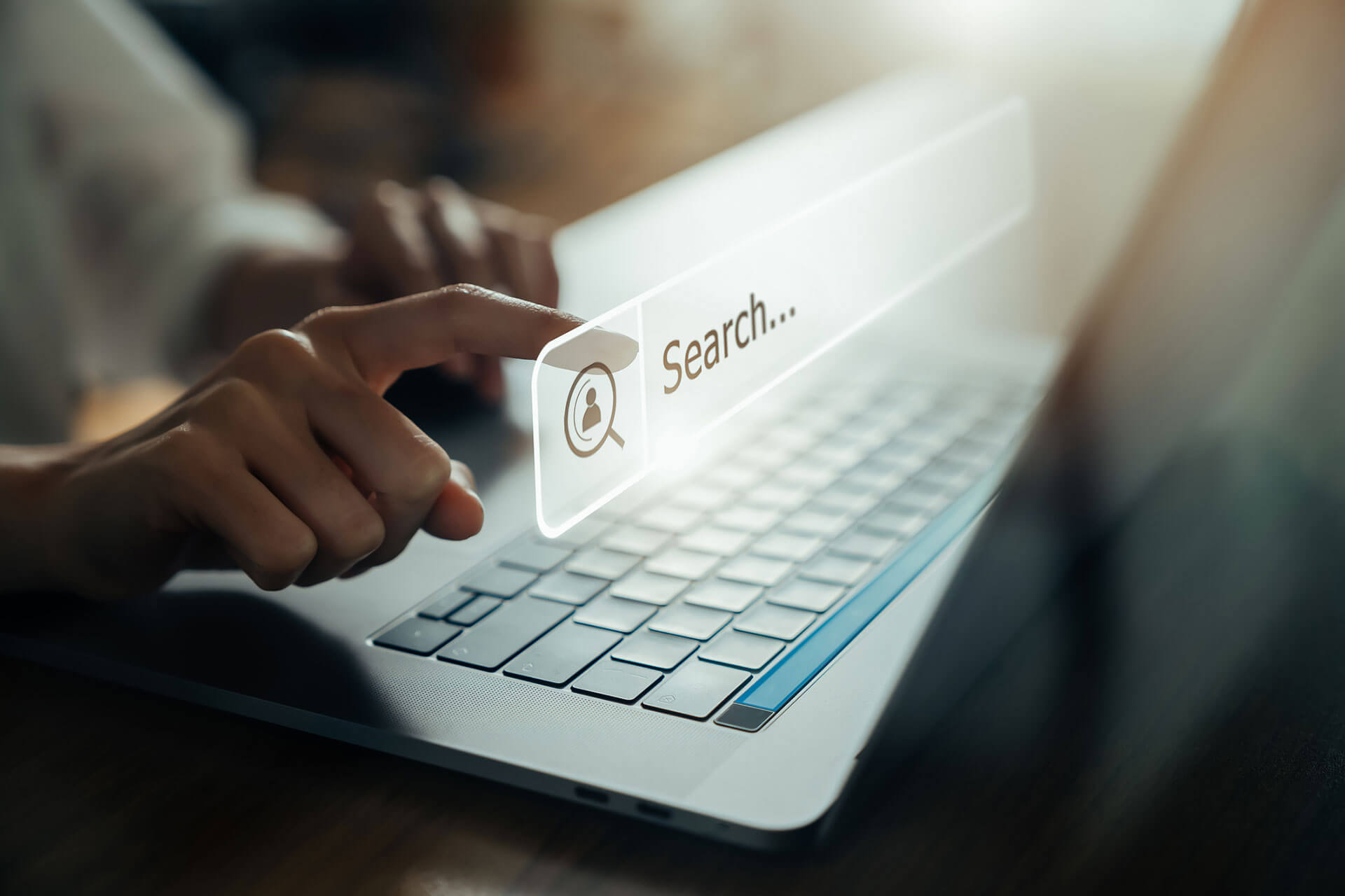 Person pointing at a hologram with the words 'search above a laptop