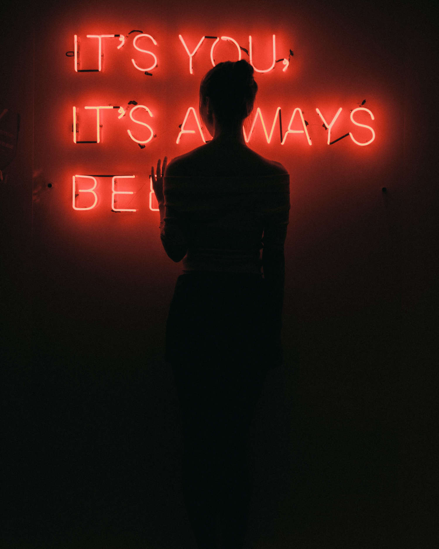 Girl posing backwards with a illuminating text on the wall.