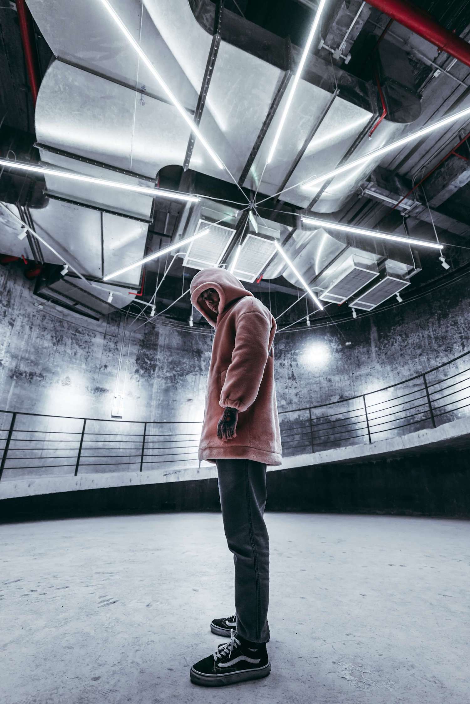 Male model wearing a pink velvet hoodie inside an industrial building.