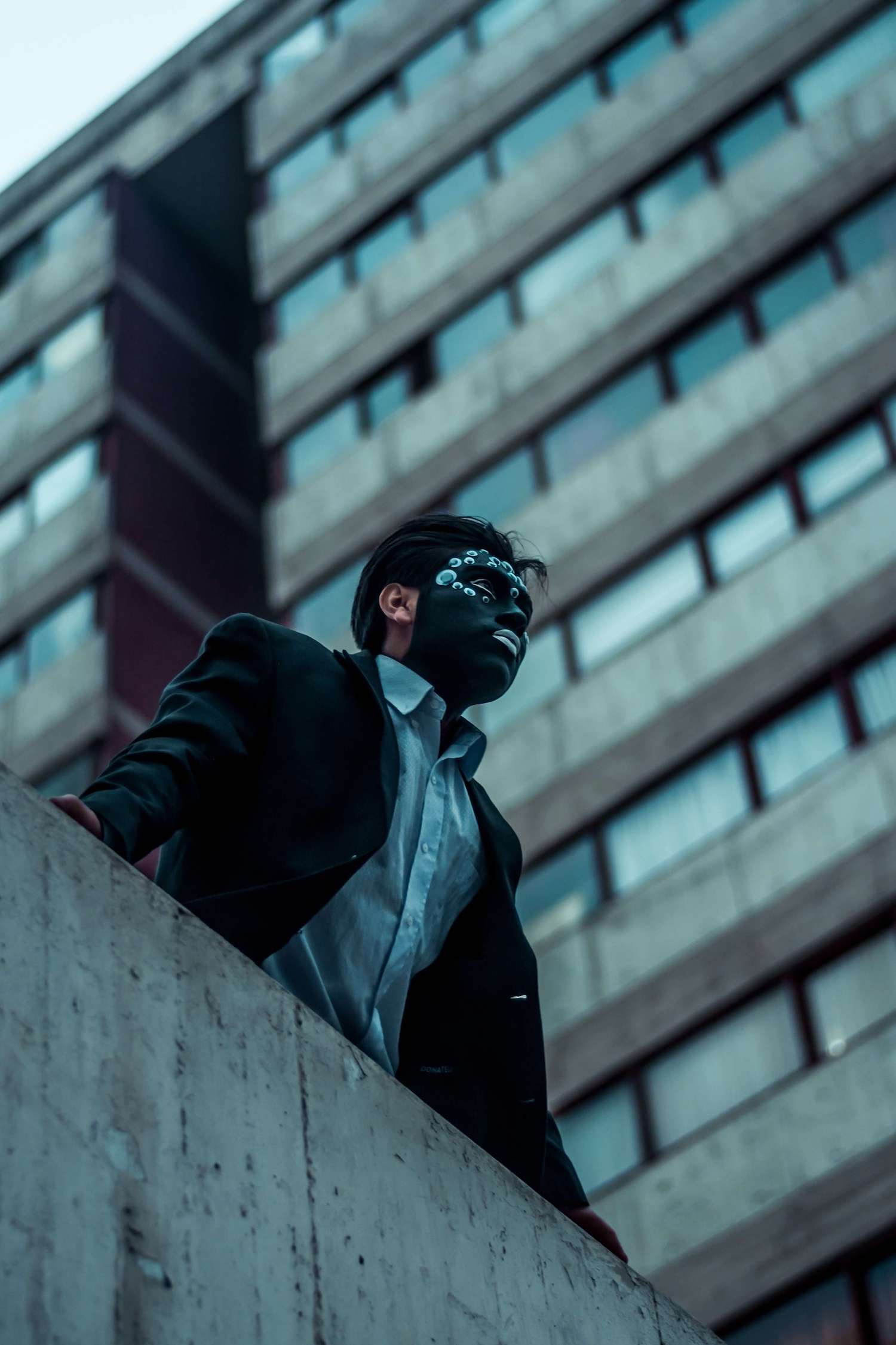 A man wearing a black decorative mask in an industrial area.