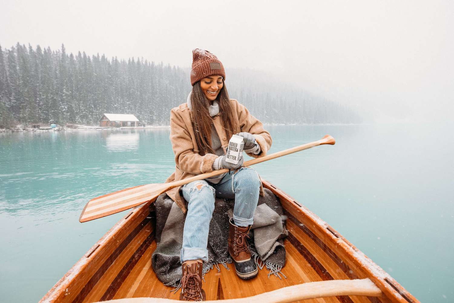 Young woman drinking boxed water in a little boat, snowing.