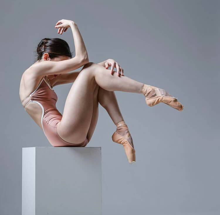Ballet dancer doing a ballet pose, seated on a stool.