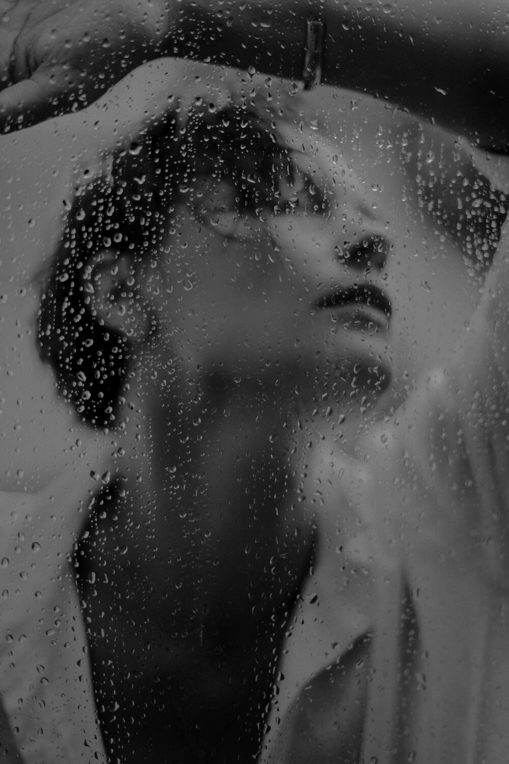 Portrait through a window with rain drops in back and white by photographer Krystsina Shyla