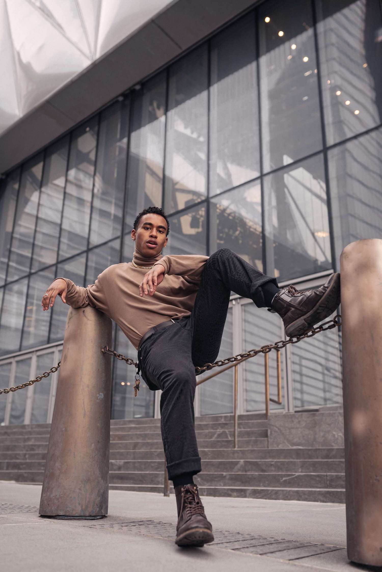 Male model sitting on a chain, glass building on the background.