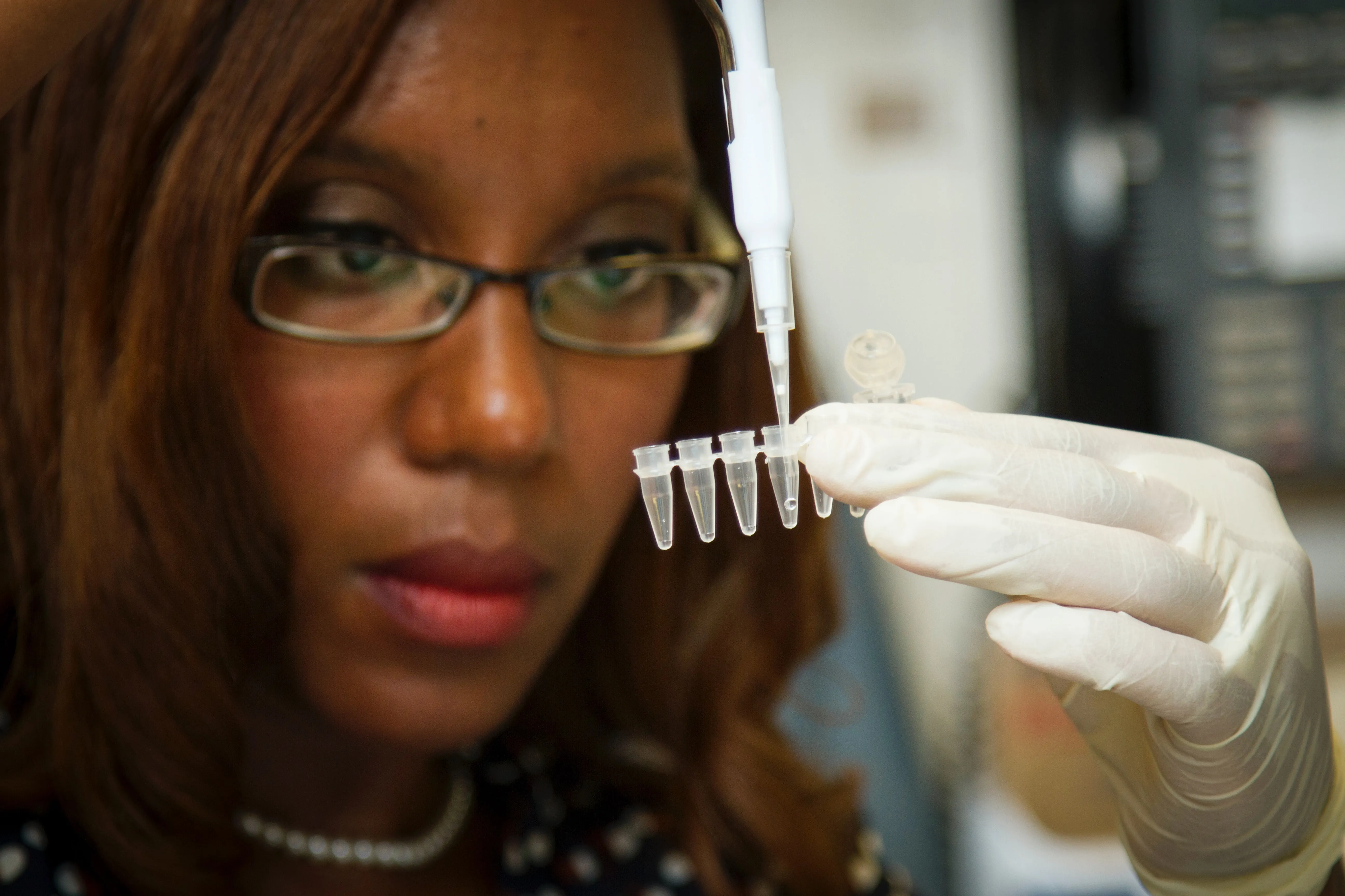 African American woman holding up small test tubes and filling with sample.