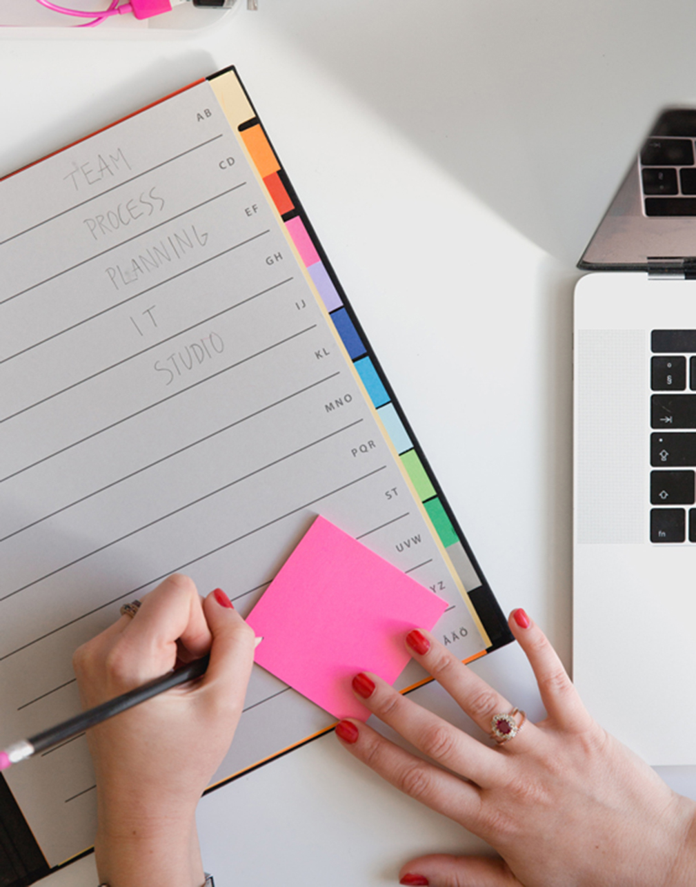 shot from above of a person writing on a sticky note with their planner and laptop