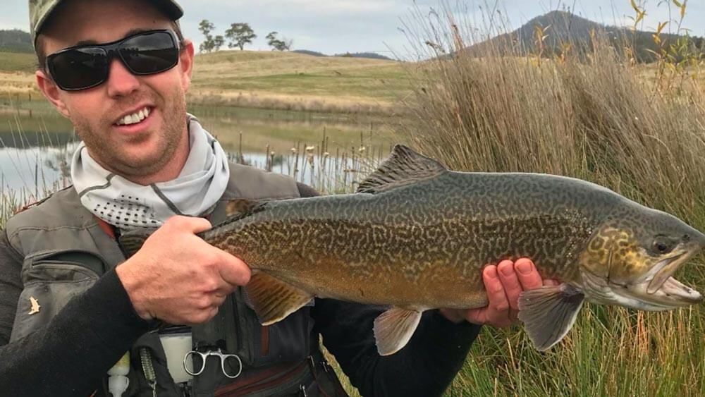 man in sunglasses holding up large trout