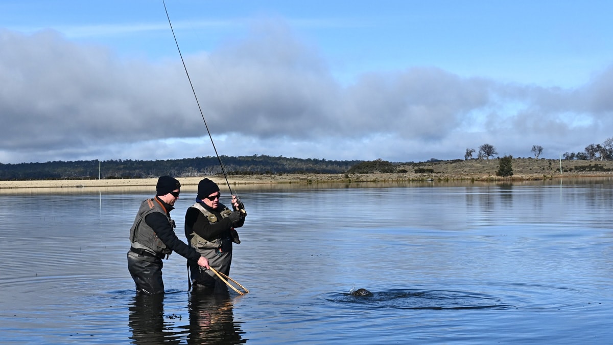 two men in fishing gear holding rod in tasmania lake